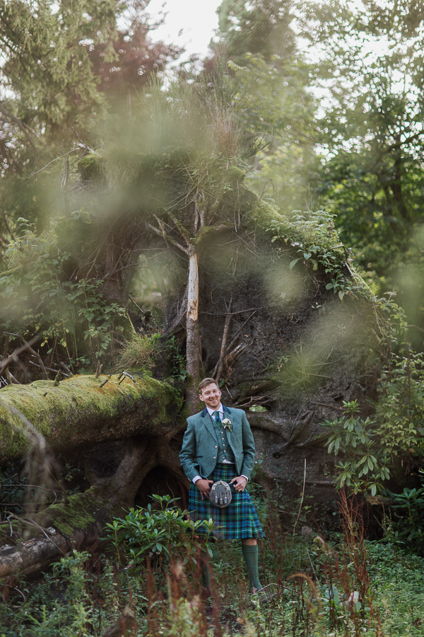 portrait of groom smiling next to a fallen tree at cameron house land