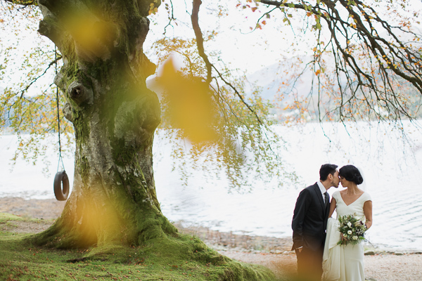 bride and groom kissing with large tree and loch in the background