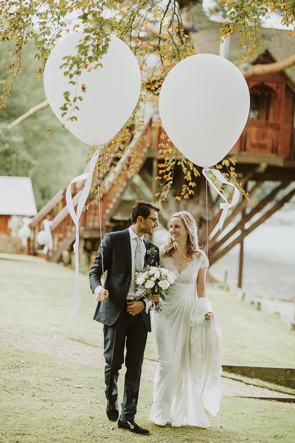 bride and groom holding large white baloons at the lodge on loch goil in scotland